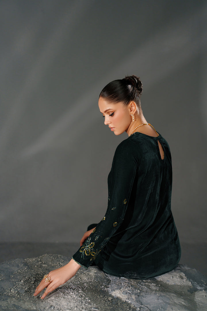 Woman in a dark green dress sitting on a textured surface with a gray background
