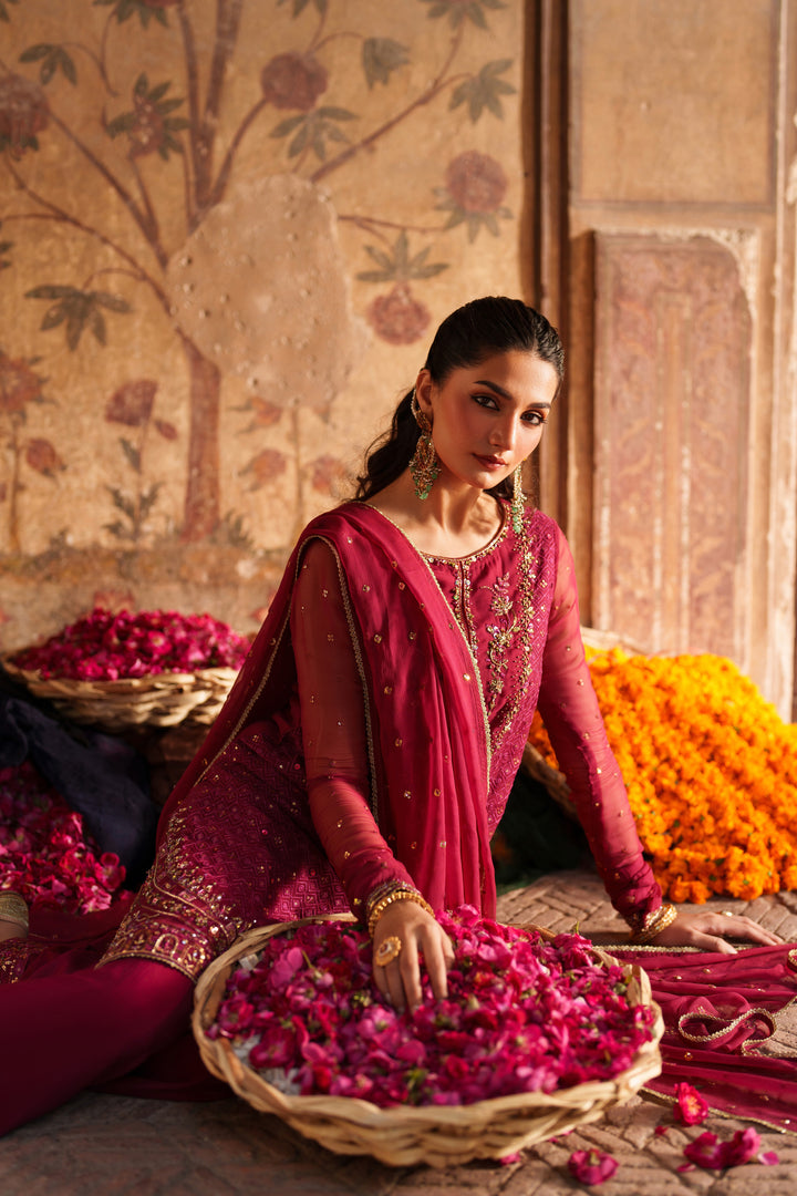 Woman in a red traditional outfit arranging flowers in a room with floral decor.