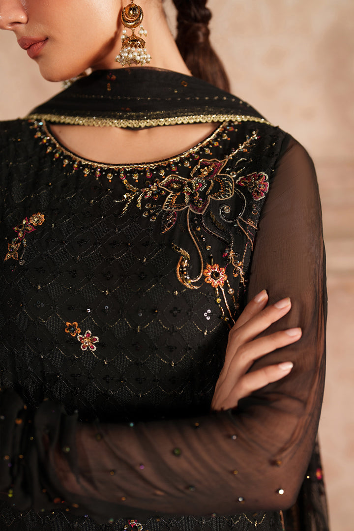 Close-up of a black embroidered garment with gold detailing on a neutral background