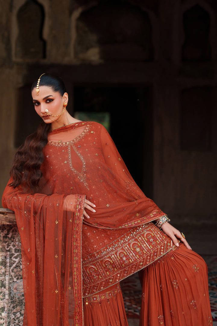 Woman in a traditional red outfit with intricate patterns, sitting against a dark background.