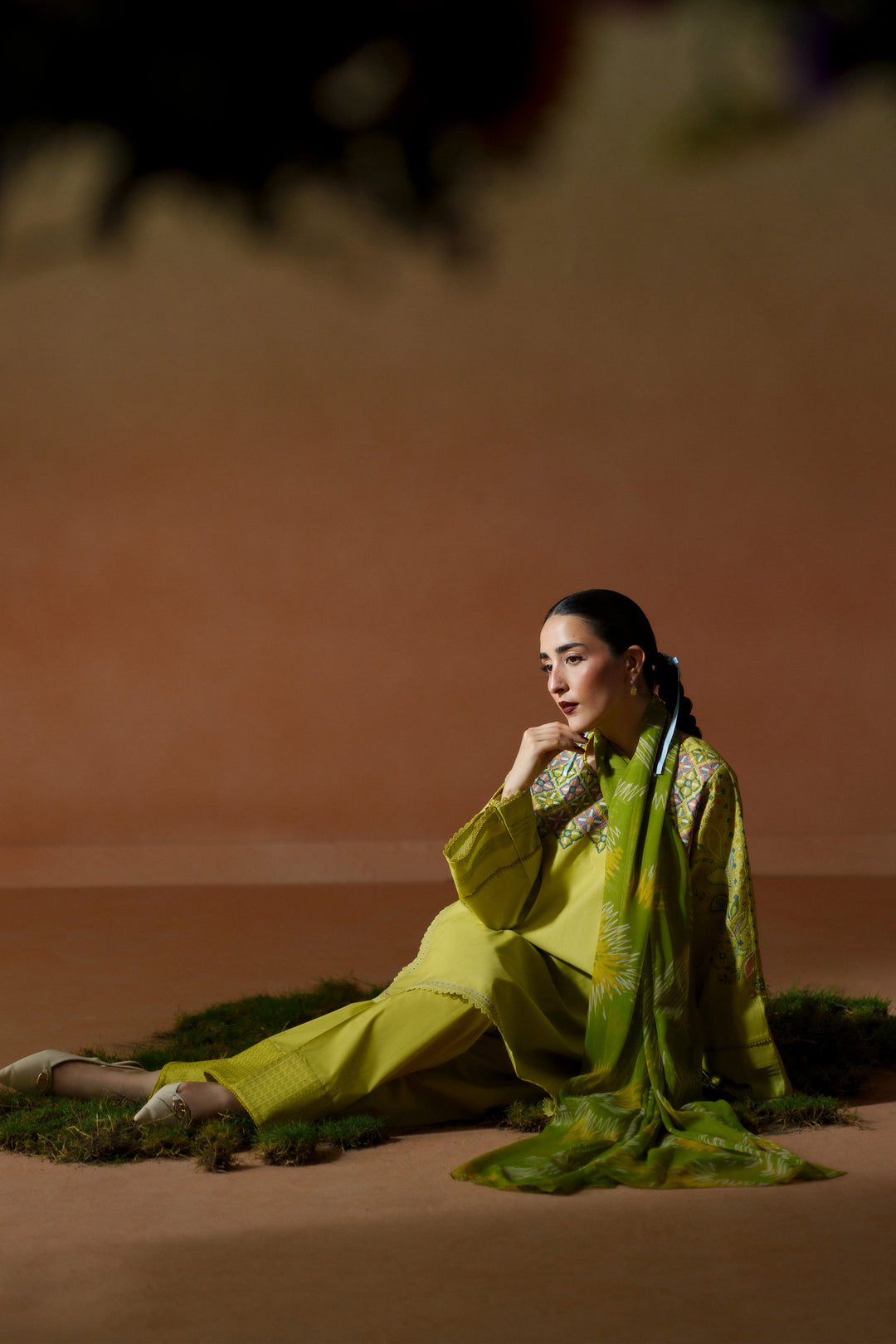 Seated pose of Deniz lime 3-piece outfit showing embroidered neckline, lace-finished sleeves, cambric shalwar, and printed dupatta.