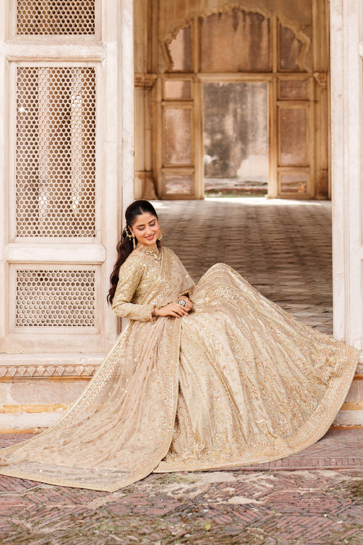 Outdoor pose of NAQSHI Ruhab ready-to-wear bridal gown in champagne gold with detailed embellishment for celebration and reception looks.