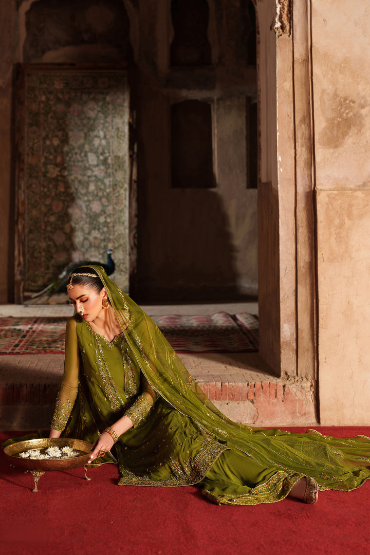 Woman in traditional green attire kneeling on a red carpet in an ornate room.