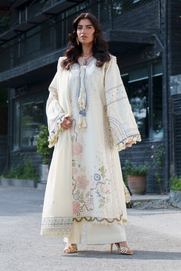 A woman models a traditional cream-colored embroidered kurta set with a matching dupatta in an outdoor urban setting with a dark building in the background.