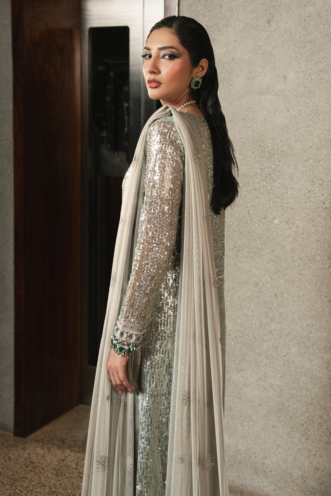 Side view of NAQSHI Urmain grey net gown highlighting elegant slit detail, adda work borders, fitted sleeves with sequins, and straight raw silk trousers.