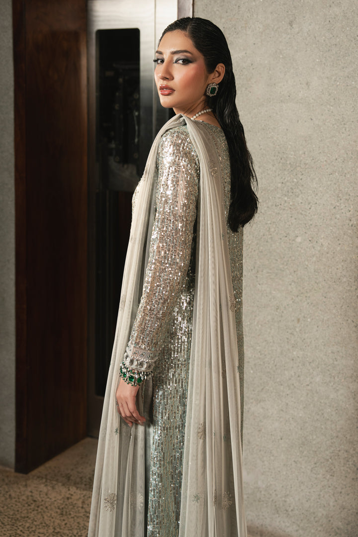 Side view of NAQSHI Urmain grey net gown highlighting elegant slit detail, adda work borders, fitted sleeves with sequins, and straight raw silk trousers.